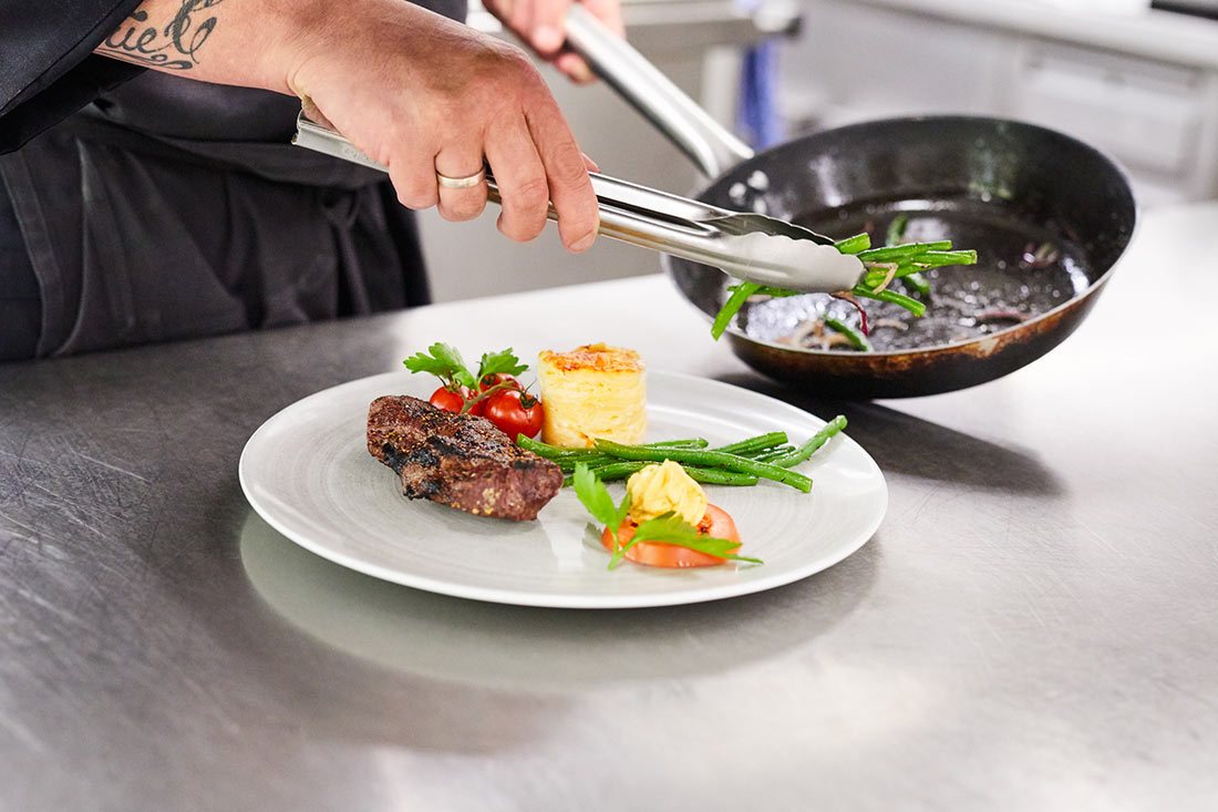 Nahaufnahme eines Tellers, der in der Küche gerade angerichtet wird.